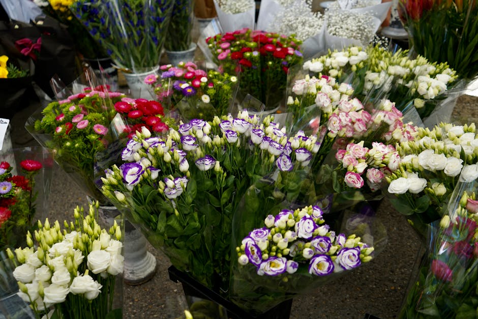 A vibrant display of fresh floral arrangements arranged on a dark surface, featuring a variety of colorful flowers including white, pink, purple, red, and green. Prominent among them are white and pur